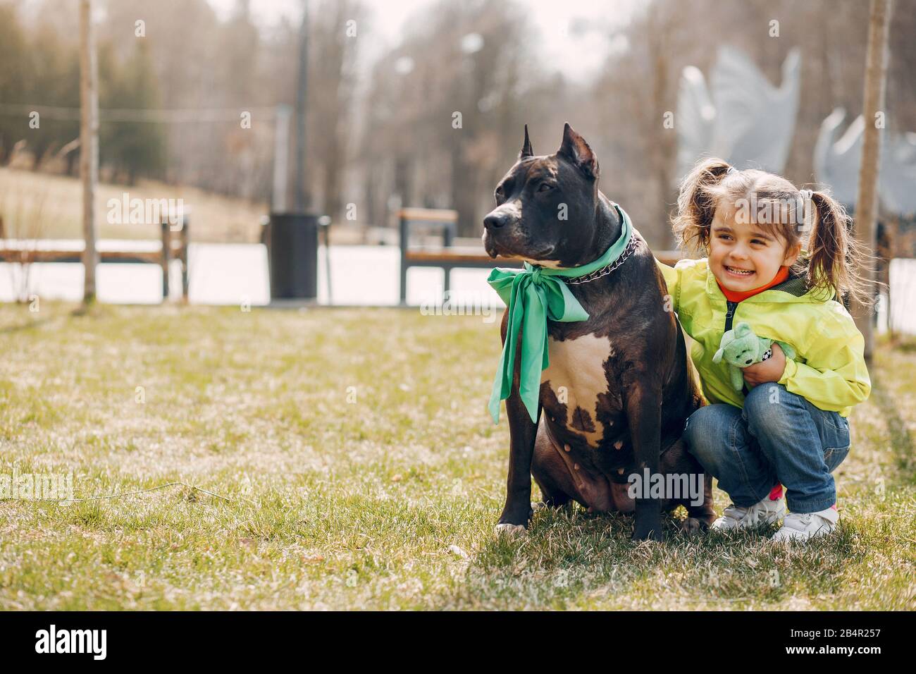 Belle petite fille dans une veste verte. Enfant dans un parc d'été avec un chien Banque D'Images