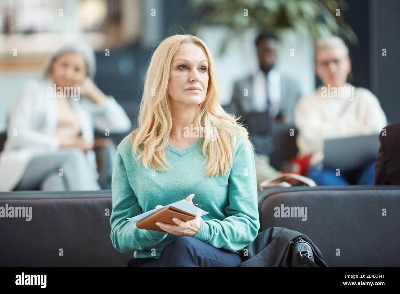 Portrait horizontal moyen d'une femme blonde mûre assise dans le salon de déture avec billet et documents à la recherche Banque D'Images