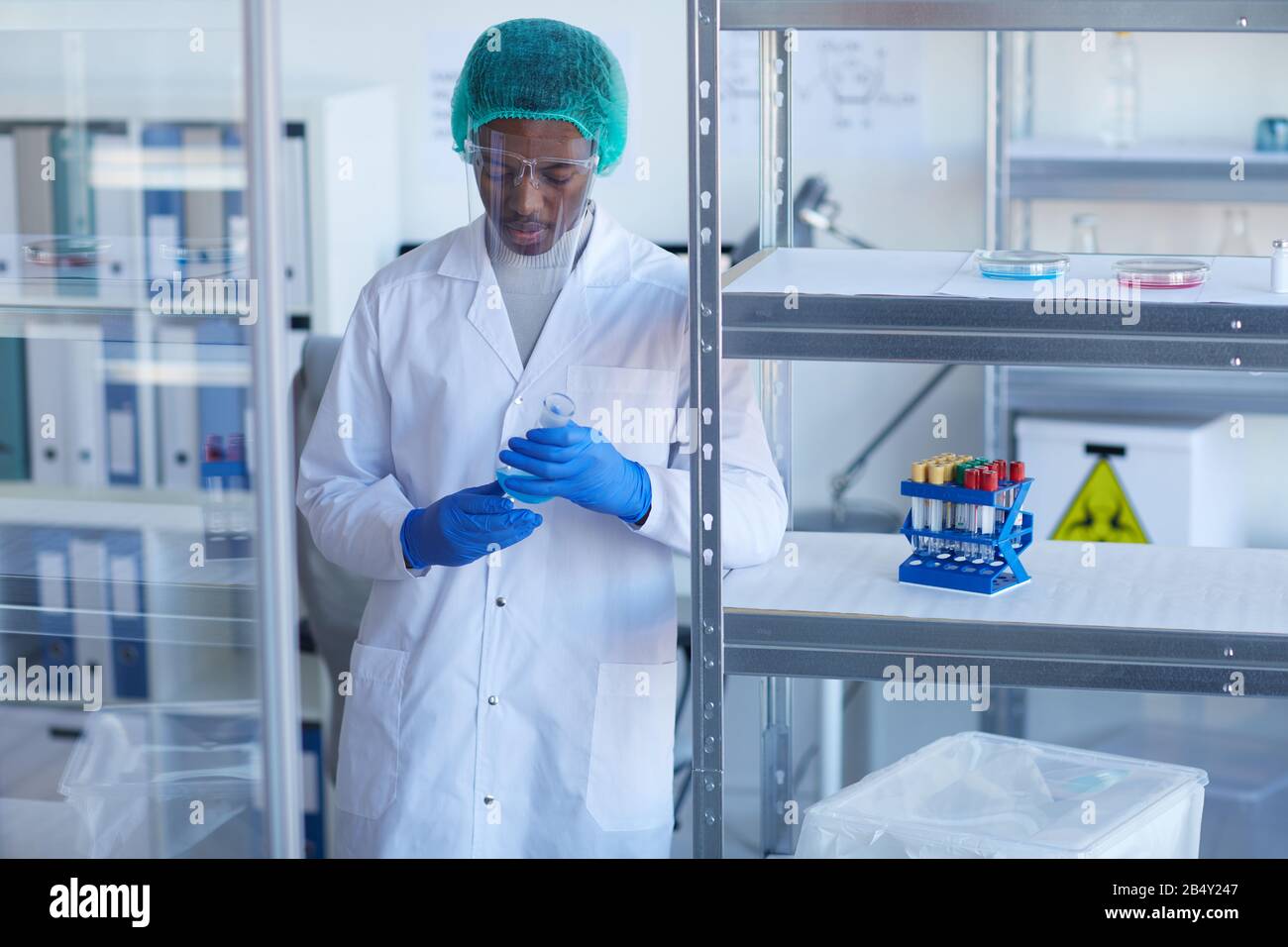 Portrait moyen horizontal d'un scientifique afro-américain en uniforme de protection travaillant en laboratoire Banque D'Images