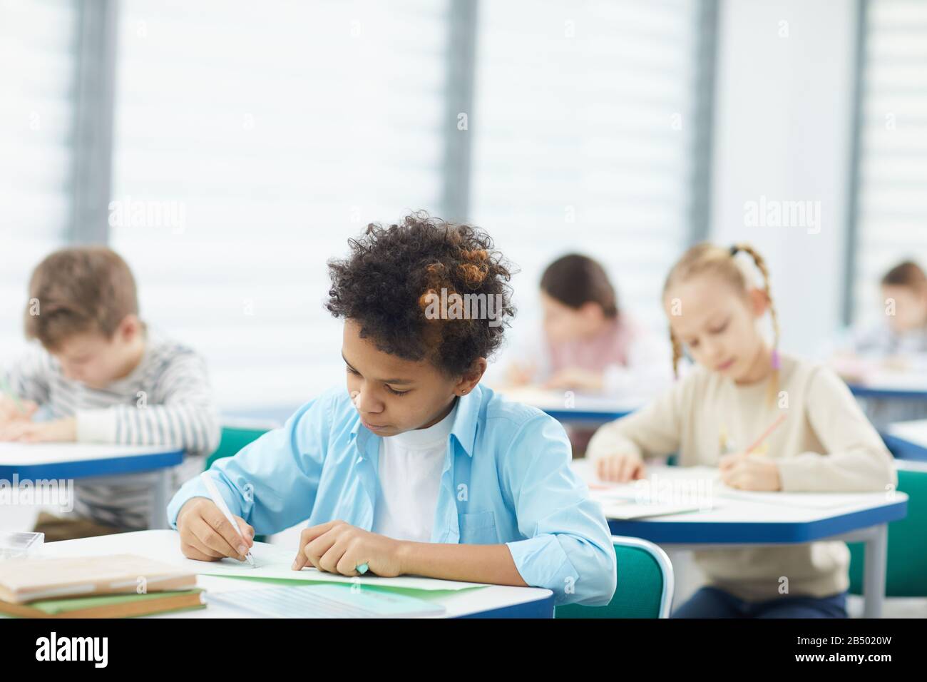 Gros plan horizontal moyen d'un garçon africain concentré assis au bureau en composition de salle de classe, espace de copie Banque D'Images