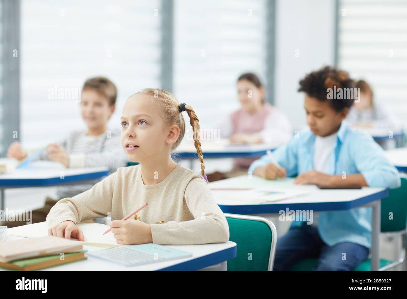 Petite fille curieuse avec cheveux blonds assis à la réception de l'école à l'écoute de son professeur, portrait horizontal, espace de copie Banque D'Images