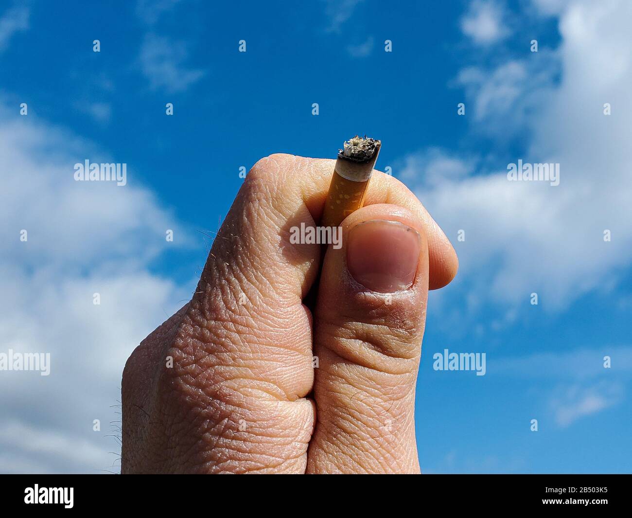 Main humaine tenir la cigarette de tabac sur fond de ciel bleu, fumer accro Banque D'Images