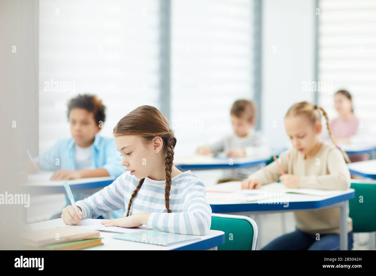 La fille caucasienne horizontale a concentré la photo des élèves de l'école primaire faisant des tâches de leçon dans la salle de classe moderne, espace de copie Banque D'Images