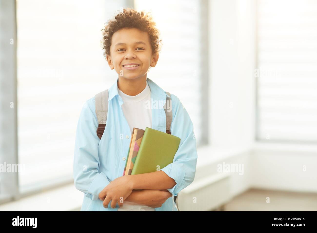 Portrait moyen horizontal de jeune écolier afro-américain portant sac à dos tenant des livres regardant l'appareil photo souriant, espace de copie Banque D'Images