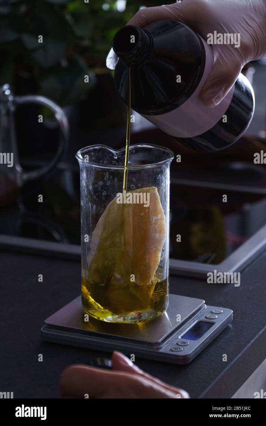 Verser à la main de l'huile de semence sur un morceau de beurre de plante dans une fiole en verre sur une balance, en préparant un mélange cosmétique de bricolage Banque D'Images