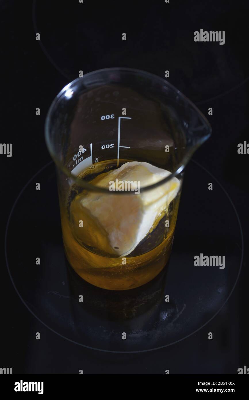 Vue de dessus du beurre solide et de l'huile à base végétale mélangé dans une fiole en verre sur la surface de la poêle en céramique Banque D'Images