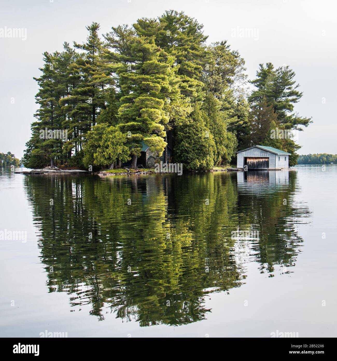 Petite île du lac Newboro, en Ontario, au Canada, avec une maison de bateaux et des arbres reflétés dans l'eau Banque D'Images