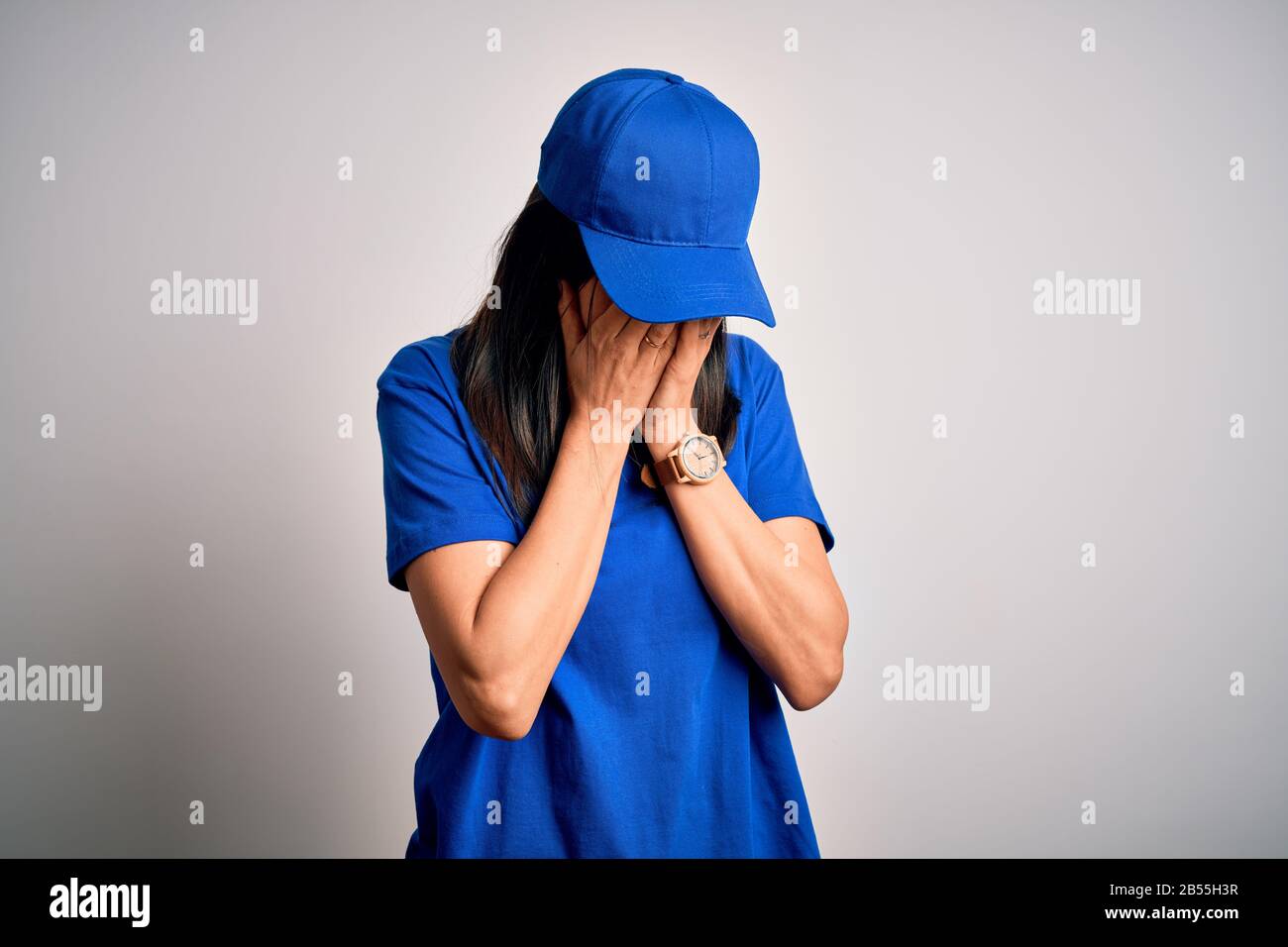 Jeune femme de livraison avec yeux bleus portant une casquette debout sur  fond bleu avec une triste expression couvrant le visage avec les mains tout  en pleurant. Dépression co Photo Stock -