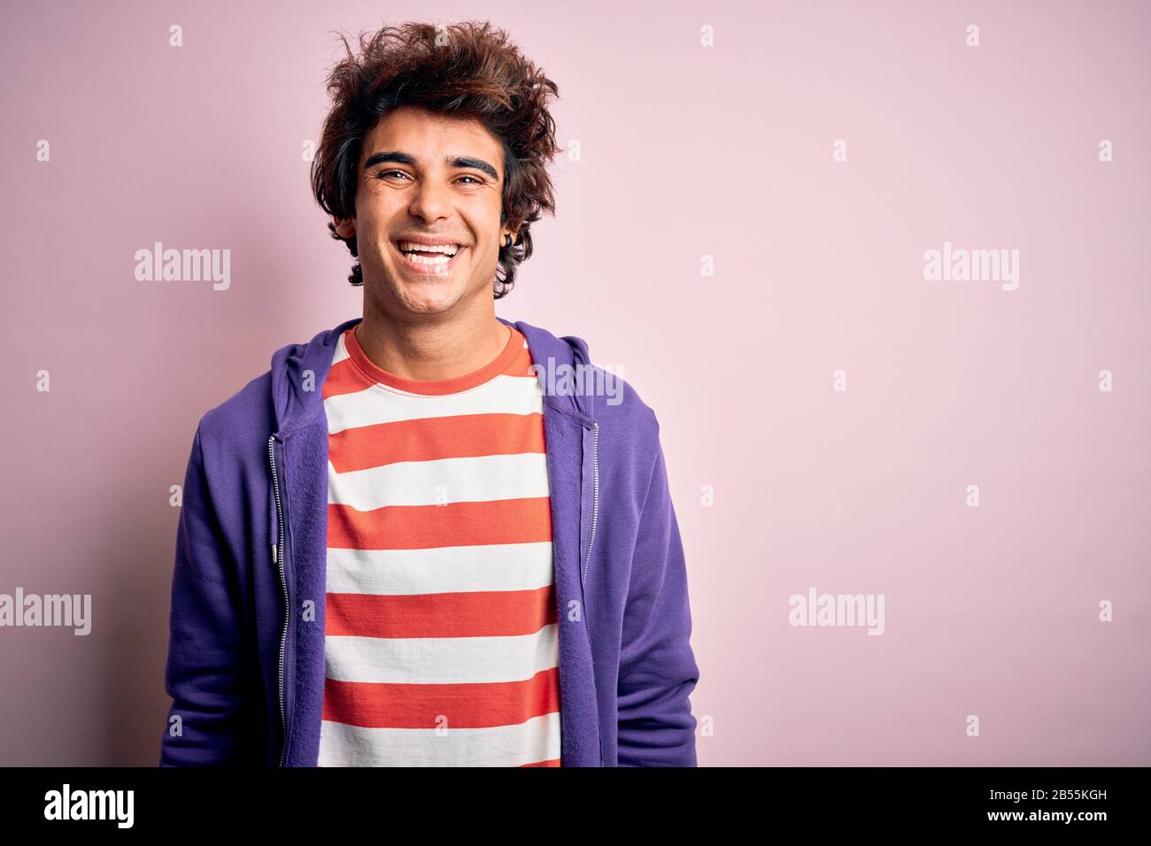 Jeune homme portant un t-shirt rayé et un sweat-shirt violet sur fond rose isolé avec un sourire heureux et frais sur le visage. Personne chanceux. Banque D'Images