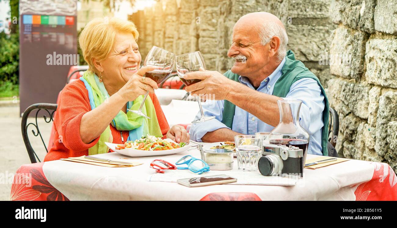 Joyeux couple senior qui applaudisse avec du vin rouge dans le restaurant italien extérieur - les personnes âgées s'amusent pendant les vacances à manger le déjeuner avec le feu arrière - L Banque D'Images