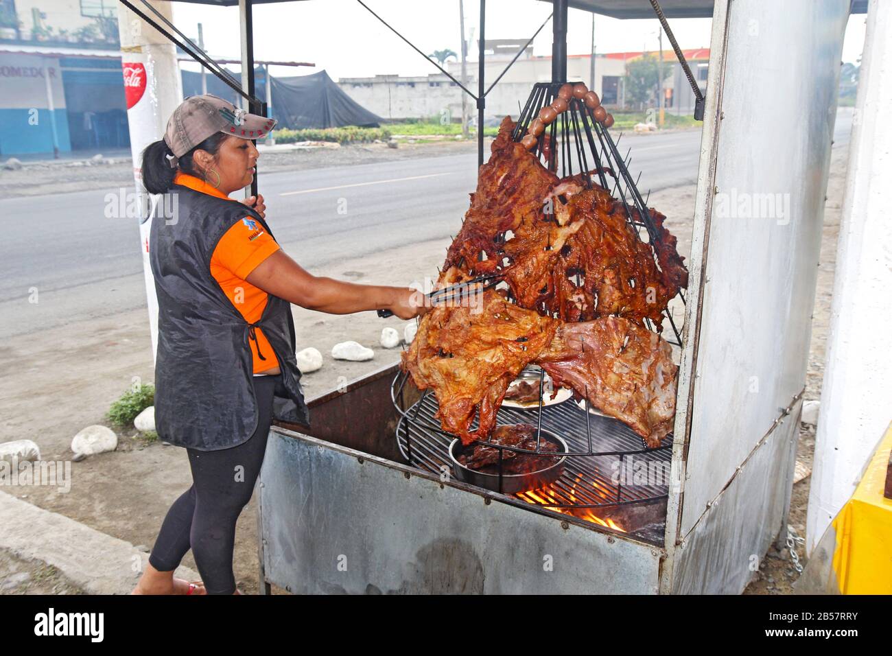 La femme a tendance à rôtir à la viande au-dessus d'un feu dans un restaurant sur le côté de la route principale à travers la ville de Naranjal en équateur. Banque D'Images