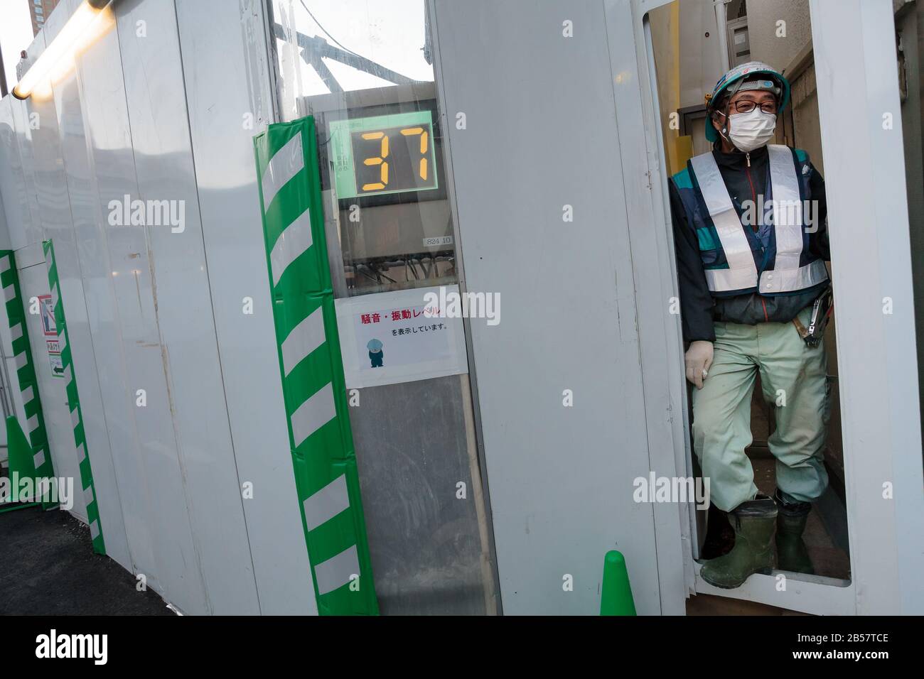 Un ouvrier de la construction mâle à la porte d'un chantier avec un compteur de décibel pour éviter la pollution sonore pendant le réaménagement de Shibuya, Tokyo, Japon Banque D'Images
