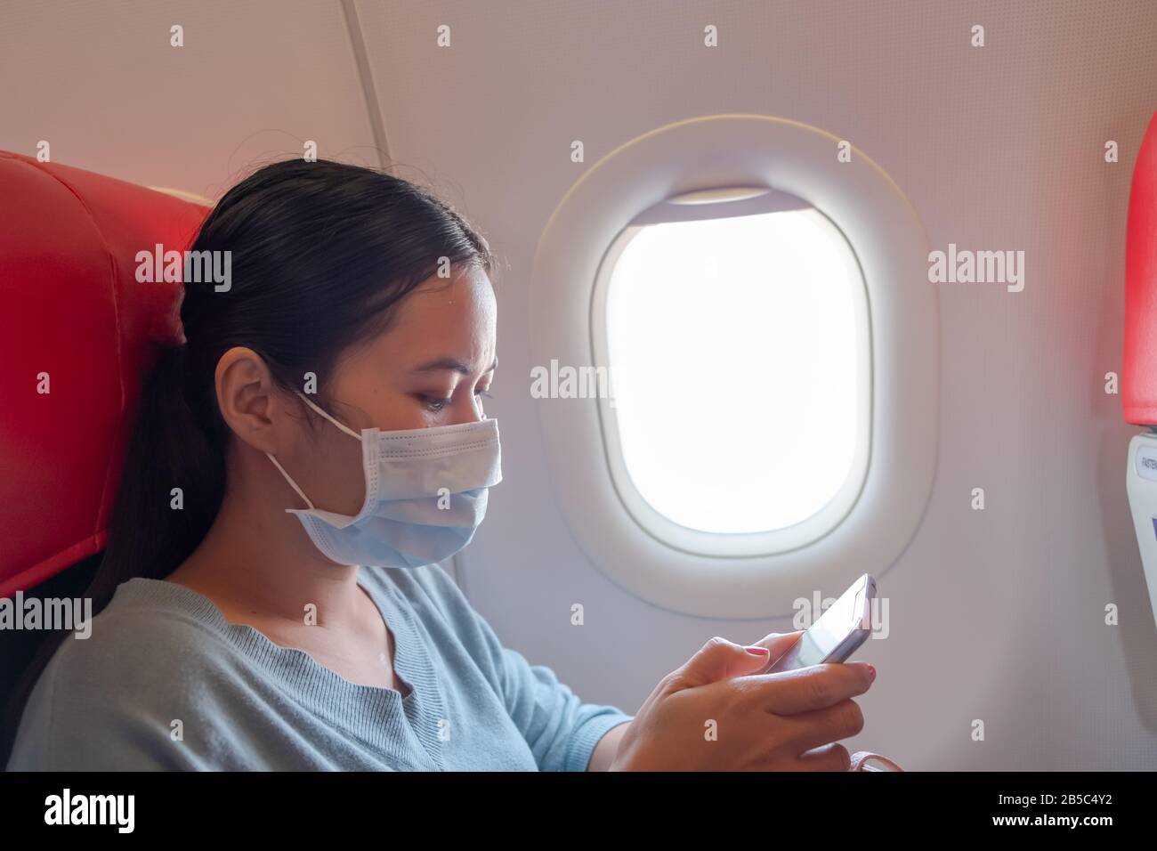 Une fille asiatique utilise un masque de protection pour le coronavirus ou le covid 19 à l'aéroport. Femme thaïlandaise jouant avec son téléphone en avion. Banque D'Images