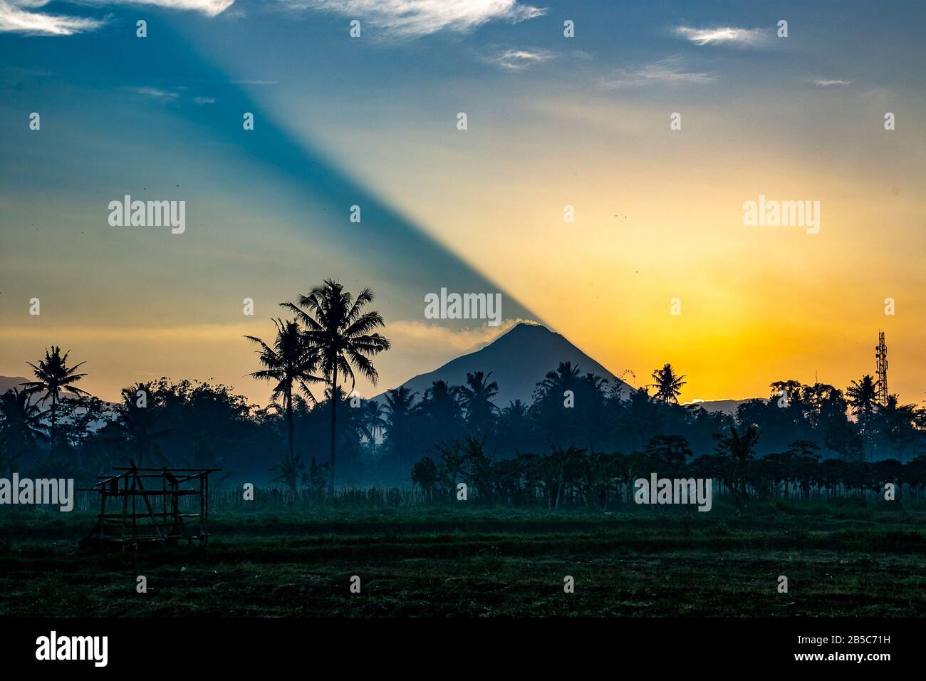 Le jette une ombre alors qu'il s'élève sur le Mont Merapi, un volcan actif à Java centrale, en Indonésie. De la fumée déborde de de la caldeira. Banque D'Images