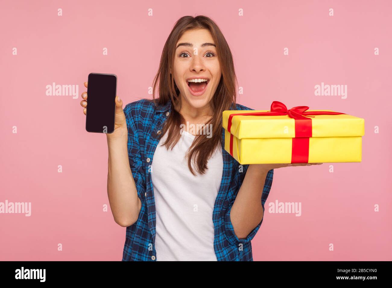 WOW, commande de livraison en ligne! Une jolie fille surprise dans une  chemise à carreaux tenant une boîte cadeau, un téléphone portable et  regardant avec étonnement, des cadeaux publicitaires et bo Photo