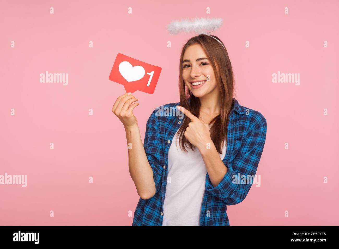 Portrait d'une charmante fille heureuse avec un halo angélique souriant et pointant sur les médias sociaux comme l'icône, bouton coeur pour profiter de contenu intéressant à la mode. Dans Banque D'Images