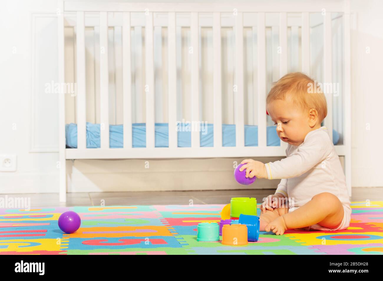 Un petit garçon de bébé s'assoit dans la chambre sur la moquette pour enfants près de la pyramide de construction de lit de bébé de blocs Banque D'Images