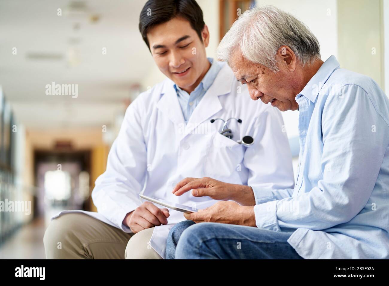 un jeune médecin asiatique souriant et sympathique parle et explique le résultat du test aux patients âgés à l'hôpital Banque D'Images