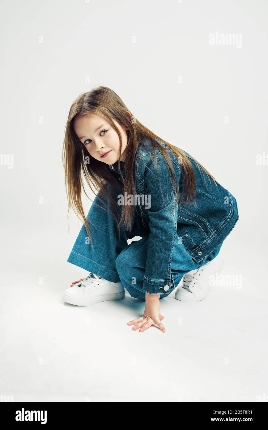 Portrait studio d'une petite fille mignonne. Enfant de mode en denim pantalon et veste et sneakers blanches. Fond gris Banque D'Images