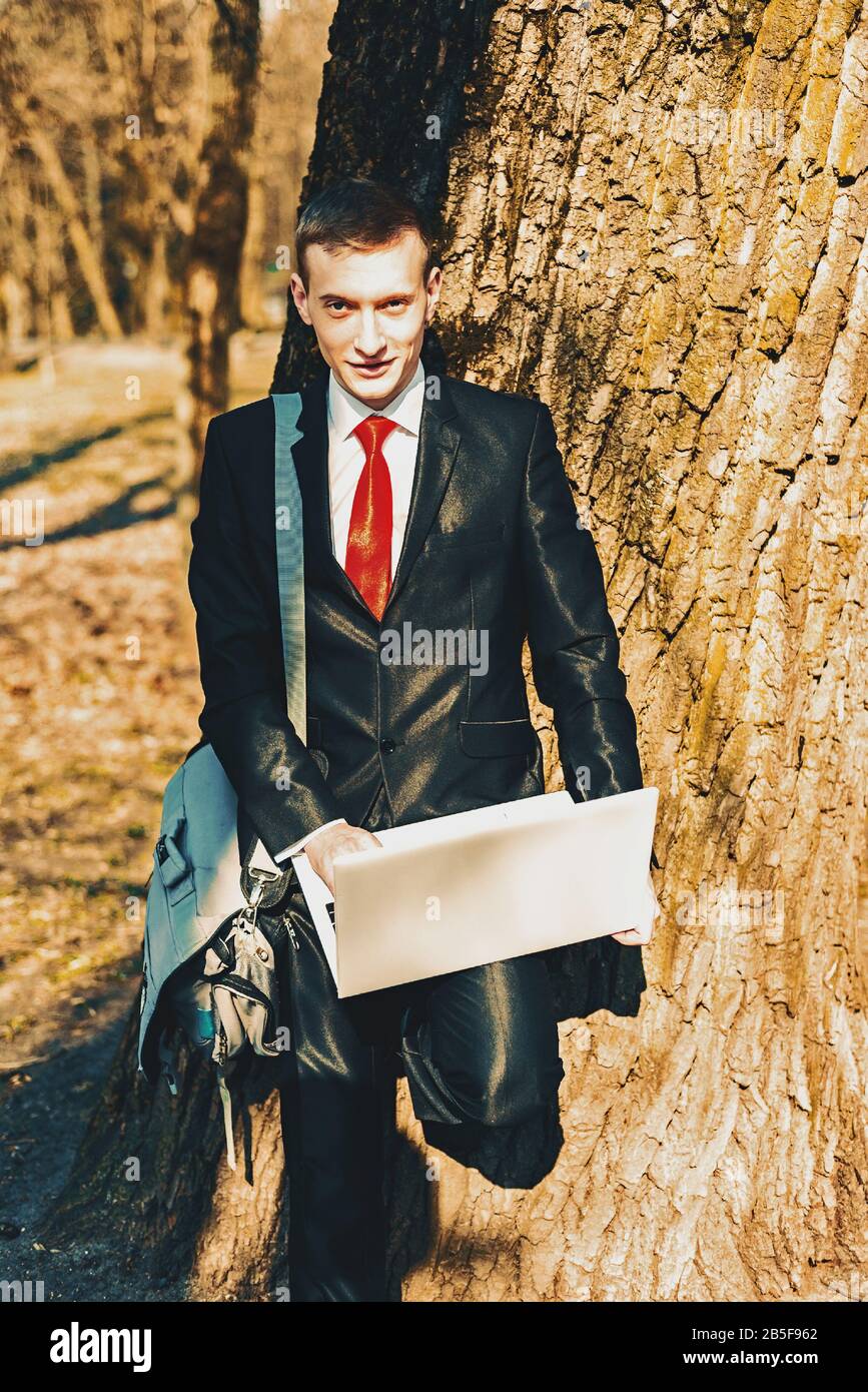 portrait d'un étudiant en costume noir et cravate rouge sur la nature près  d'un grand arbre. sur l'épaule d'un jeune sac de type. indépendant tient un  ordinateur portable Photo Stock - Alamy