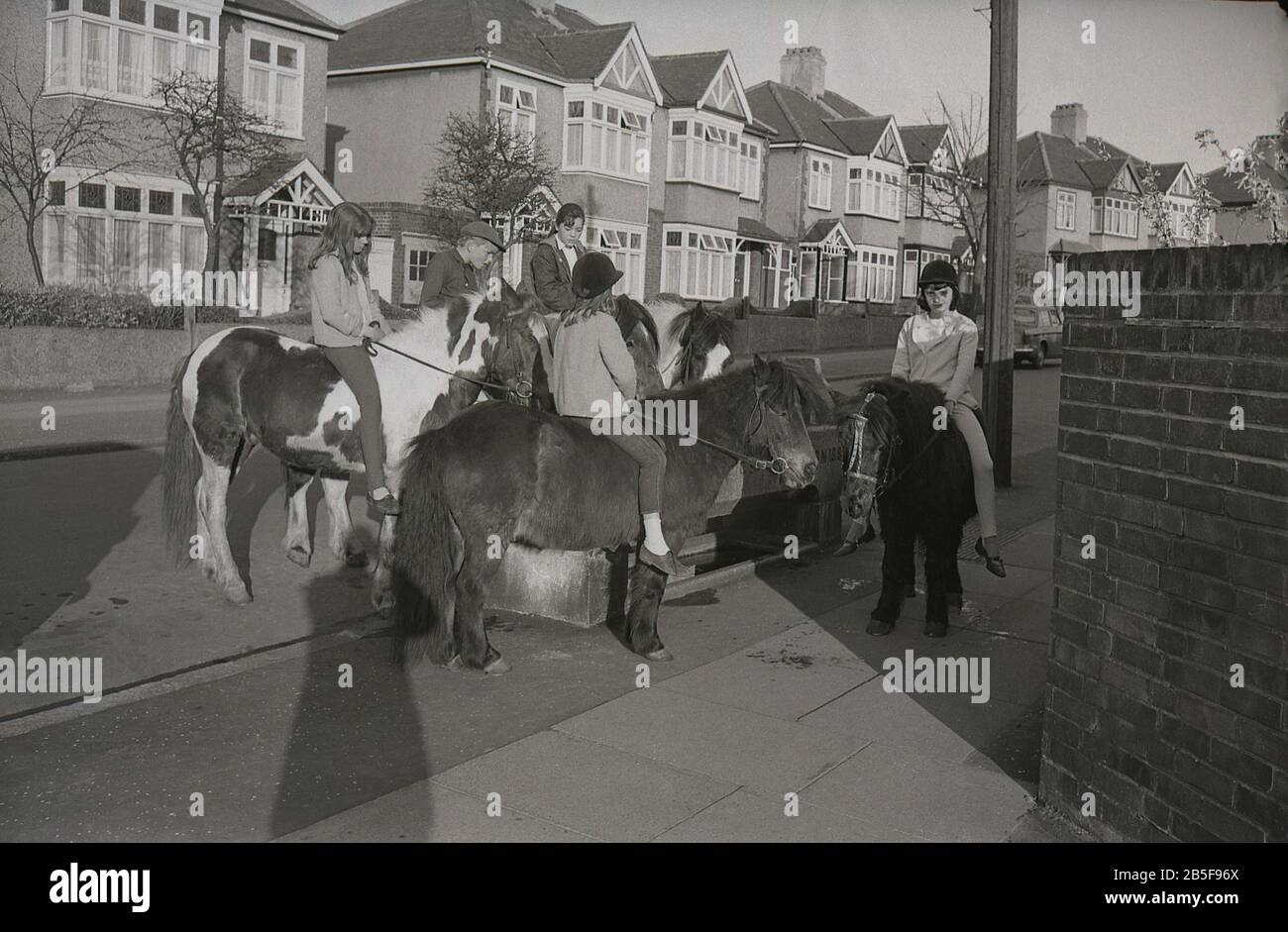 Années 1970, historique, dans une rue de banlieue, les jeunes sur les chevaux et les poneys s'arrêtent à un abreuvoir pour donner à leurs animaux un rafraîchissement, au sud de Londres, en Angleterre, pendant un été particulièrement chaud. Au cours de la décennie, certains d'entre eux étaient extrêmement chauds. Banque D'Images