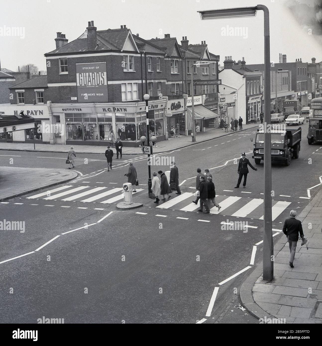 1960, historique, policier tenant un camion sur Eltham High Street, dans le sud de Londres, afin que les gens puissent traverser la route sur un passage à niveau. Banque D'Images
