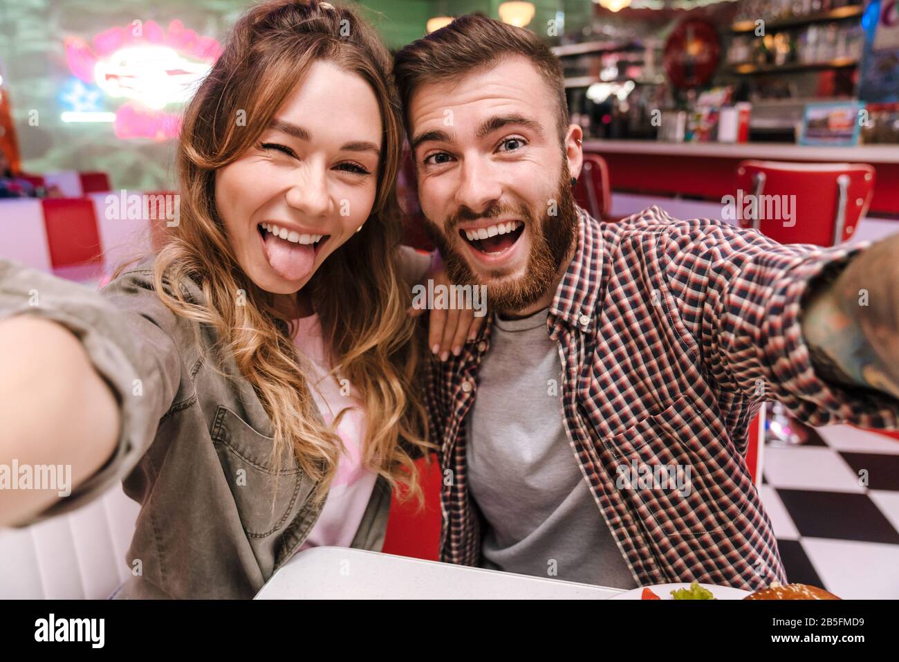 Image d'un joli jeune couple amoureux dans un café de cuisine rétro et lumineux de rue prendre un selfie par appareil photo montrant la langue. Banque D'Images
