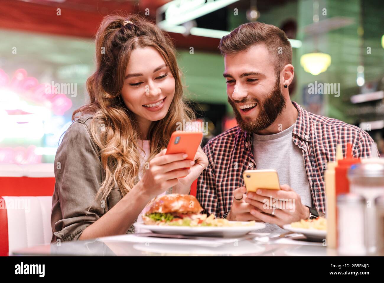 Photo d'un jeune couple charmant et optimiste dans un café de cuisine de rue rétro lumineux utilisant le téléphone mobile. Banque D'Images