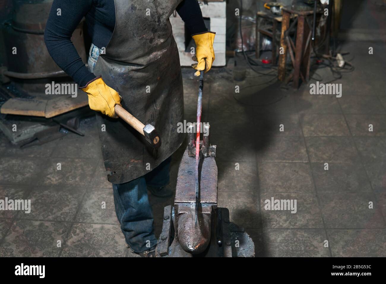 les mains femelles forgent une pièce métallique chaude sur l'enclume dans une forge traditionnelle Banque D'Images
