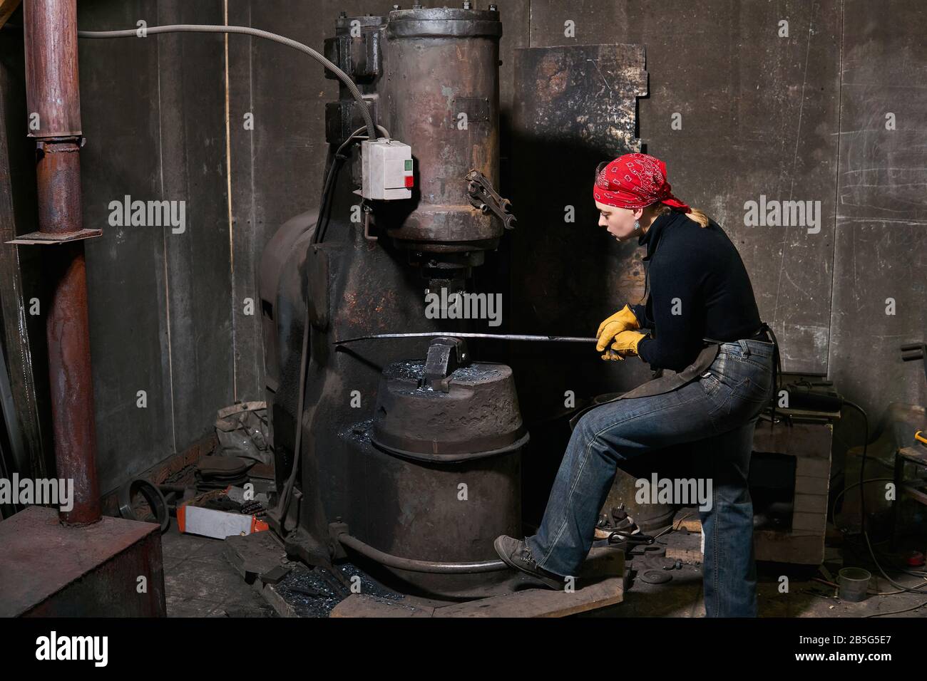 femme forgeron traite une pièce chaude avec un marteau électrique dans un atelier Banque D'Images