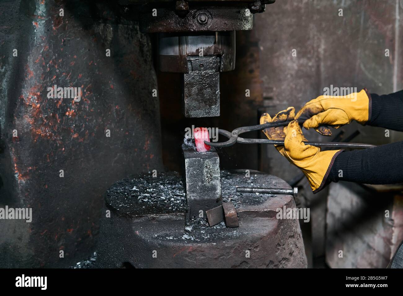 femme forgeron traite une pièce chaude rouge avec un marteau électrique dans un atelier Banque D'Images