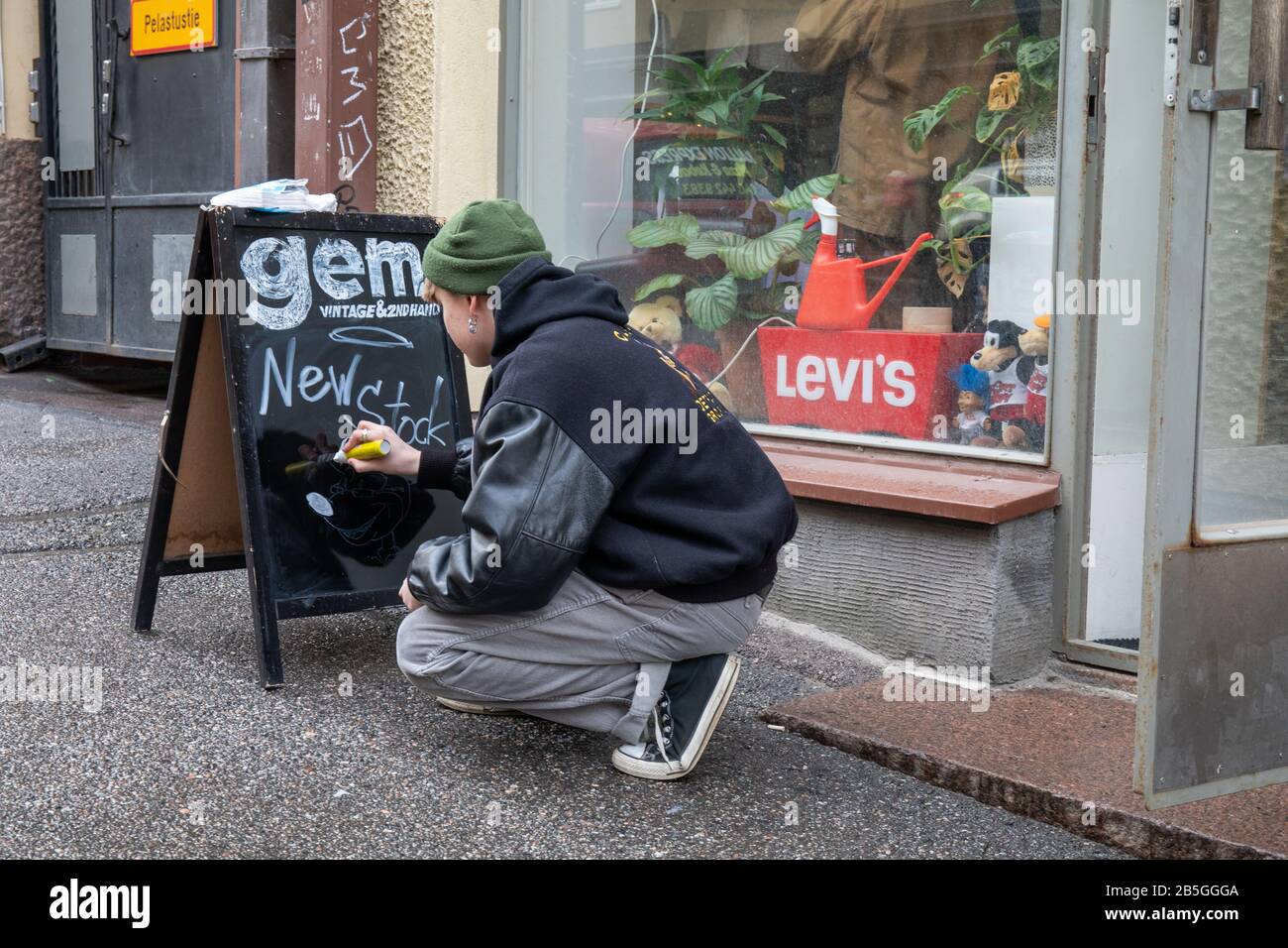 Jeune homme écrivant sur le tableau noir du trottoir devant le magasin d'occasion et de deuxième main Gem dans le district de Kallio à Helsinki, Finlande Banque D'Images