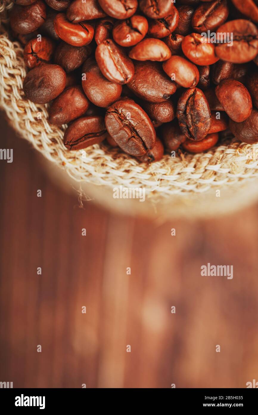 Grains de café se rapprochez dans un sac de burlap sur fond en bois. Contraste doux. Grains de café torréfiés aromatiques. La vue du haut. Macro Banque D'Images