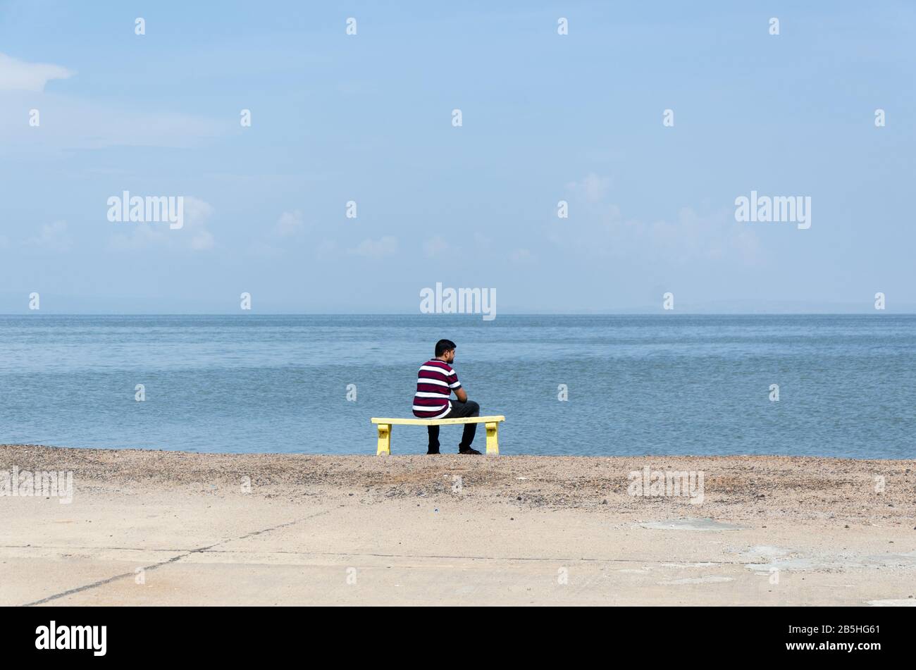 Seul, un seul garçon assis sur un banc, en regardant la vaste étendue du désert blanc submergé pendant la saison de mousson à Dhordo, Kutch, Gujarat, Inde Banque D'Images