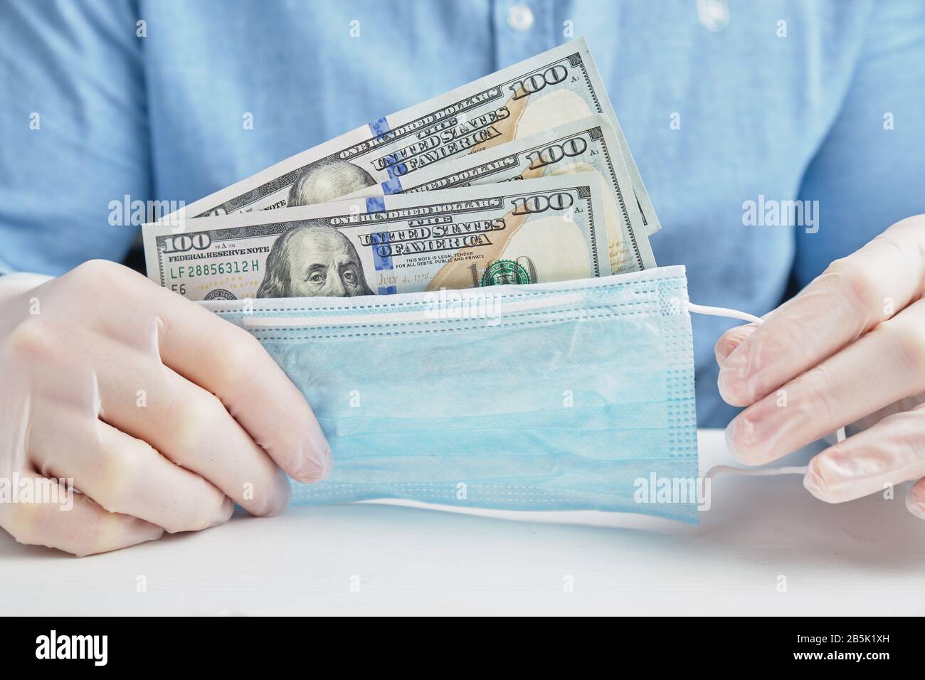 Une main en gants contient un masque médical de protection avec des dollars. Le concept d'affaires et beaucoup d'argent sur la protection. Gros plan. Banque D'Images