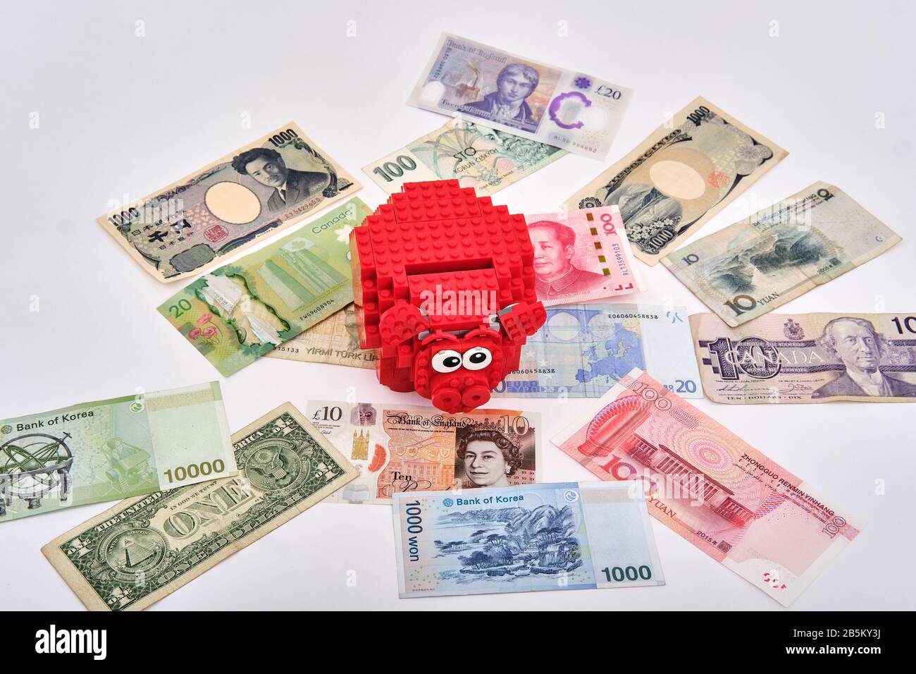 Banque de porc lego rouge assemblée entourée de différentes devises billets en papier du monde entier Banque D'Images