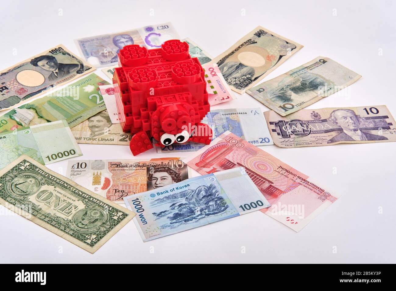 Banque de porc lego rouge assemblée entourée de différentes devises billets en papier du monde entier Banque D'Images