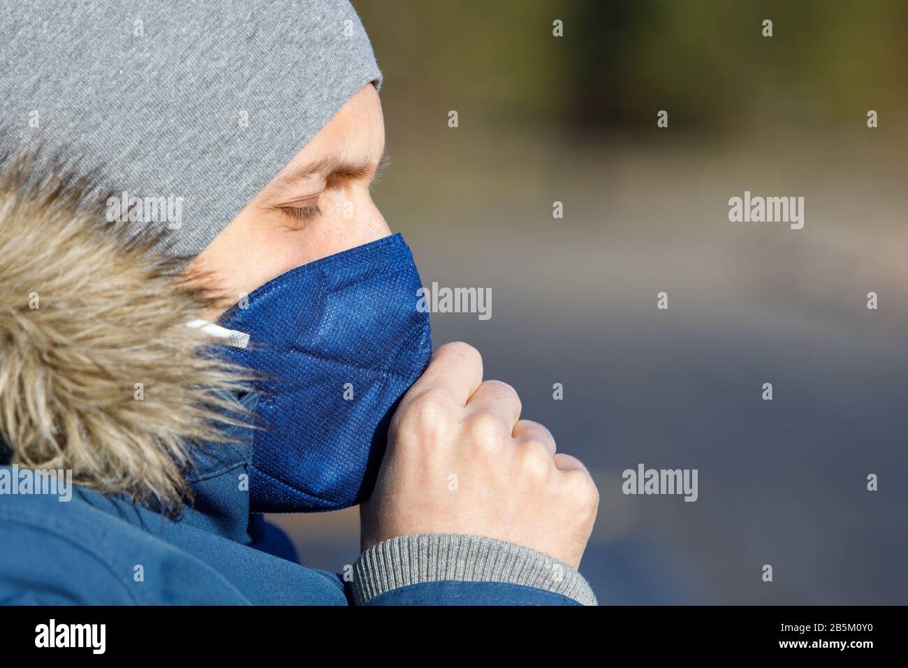 Gros plan d'homme malade dans une veste bleue avec une capuche ayant un froid, toussant et portant un masque médical, vue latérale, espace de copie. Épidémie de grippe, poussière aller Banque D'Images