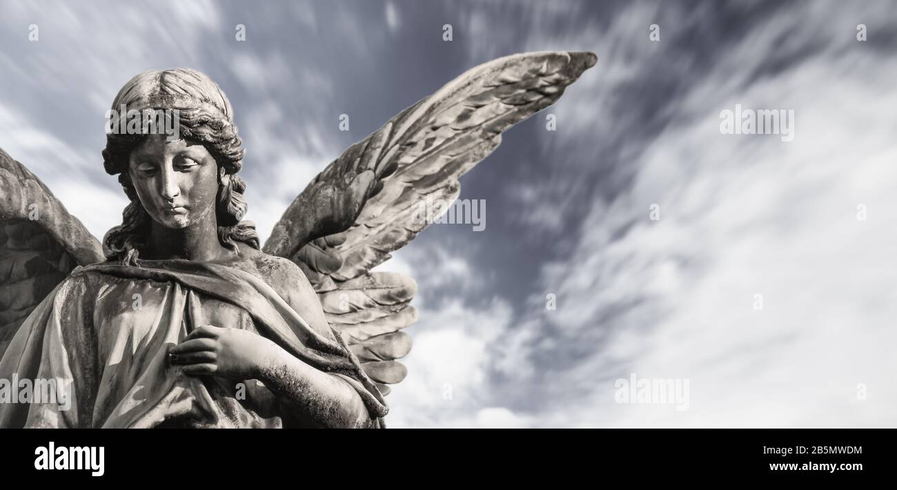 Triste sculpture d'ange gardien avec ailes ouvertes isolées avec des nuages blancs flous ciel dramatique. Sorrow ange triste expression sculpture avec les yeux vers le bas et Banque D'Images
