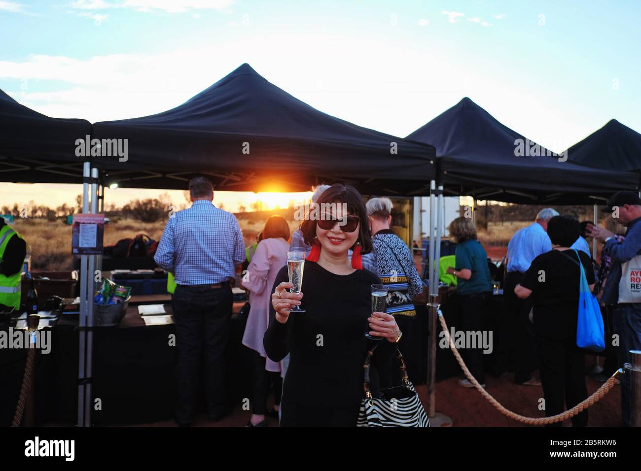 Femme avec un verre de vin mousseux à l'Opéra dans l'Outback à Uluru et au champ de lumière, sous le gala de l'Opéra Inaugural des étoiles de l'Outback Banque D'Images