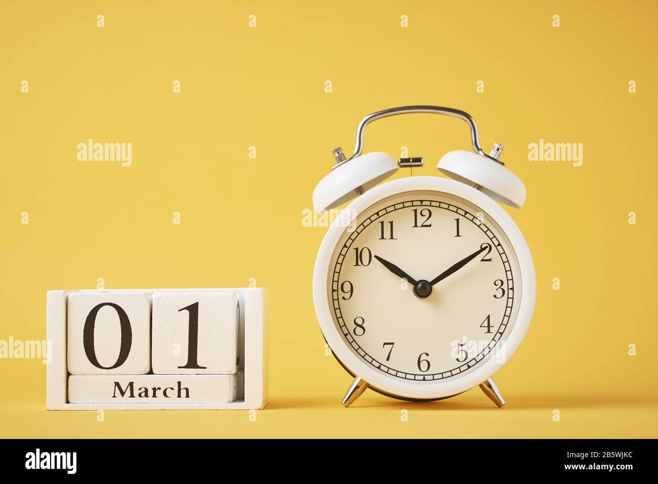 Réveil rétro blanc avec cloches et blocs calendrier en bois avec date du 1er mars sur fond jaune Banque D'Images