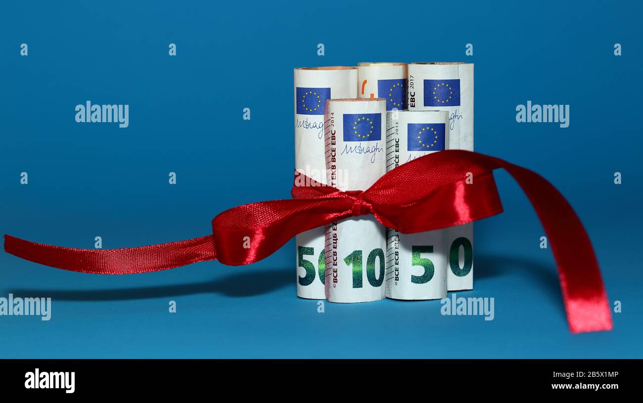 Billets de 50, 10 et 5 euros roulés en rouleaux attachés avec noeud décoratif en ruban rouge près isolé sur fond bleu, concept de cadeau économique Banque D'Images