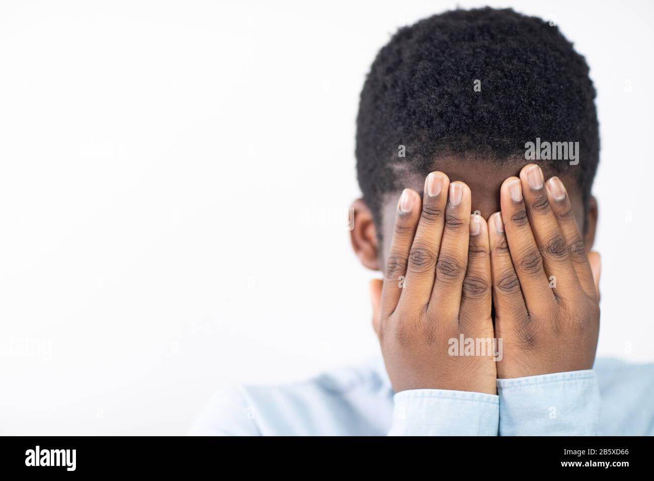 Garçon Mécontent Couvrant Le Visage Avec Les Mains Contre Le Fond Blanc Banque D'Images