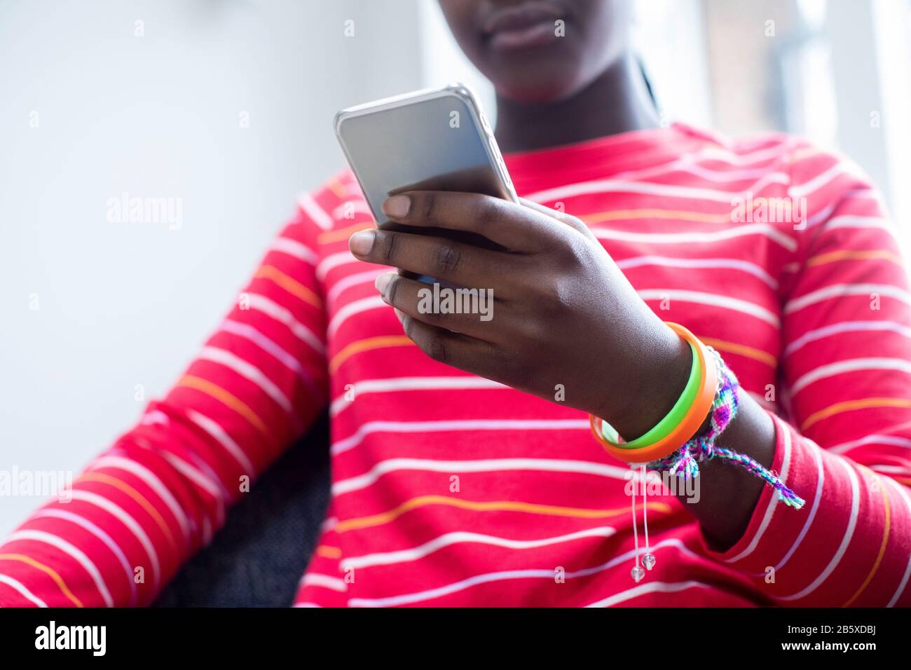 Gros Plan De Teenage Girl Portant Des Bracelets En Utilisant Le Téléphone Mobile À La Maison Banque D'Images