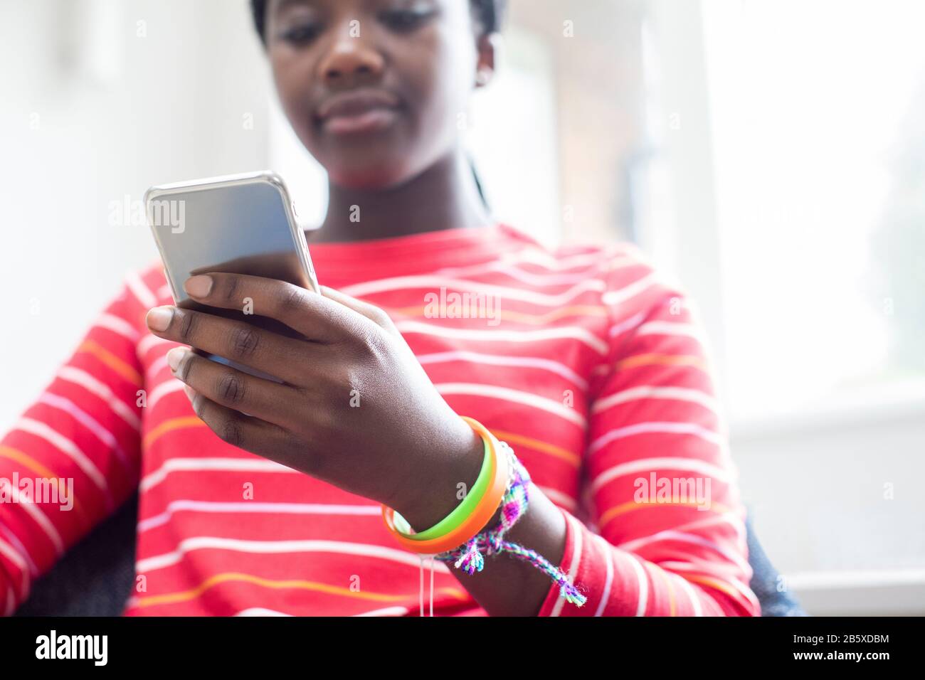 Gros Plan De Teenage Girl Portant Des Bracelets En Utilisant Le Téléphone Mobile À La Maison Banque D'Images
