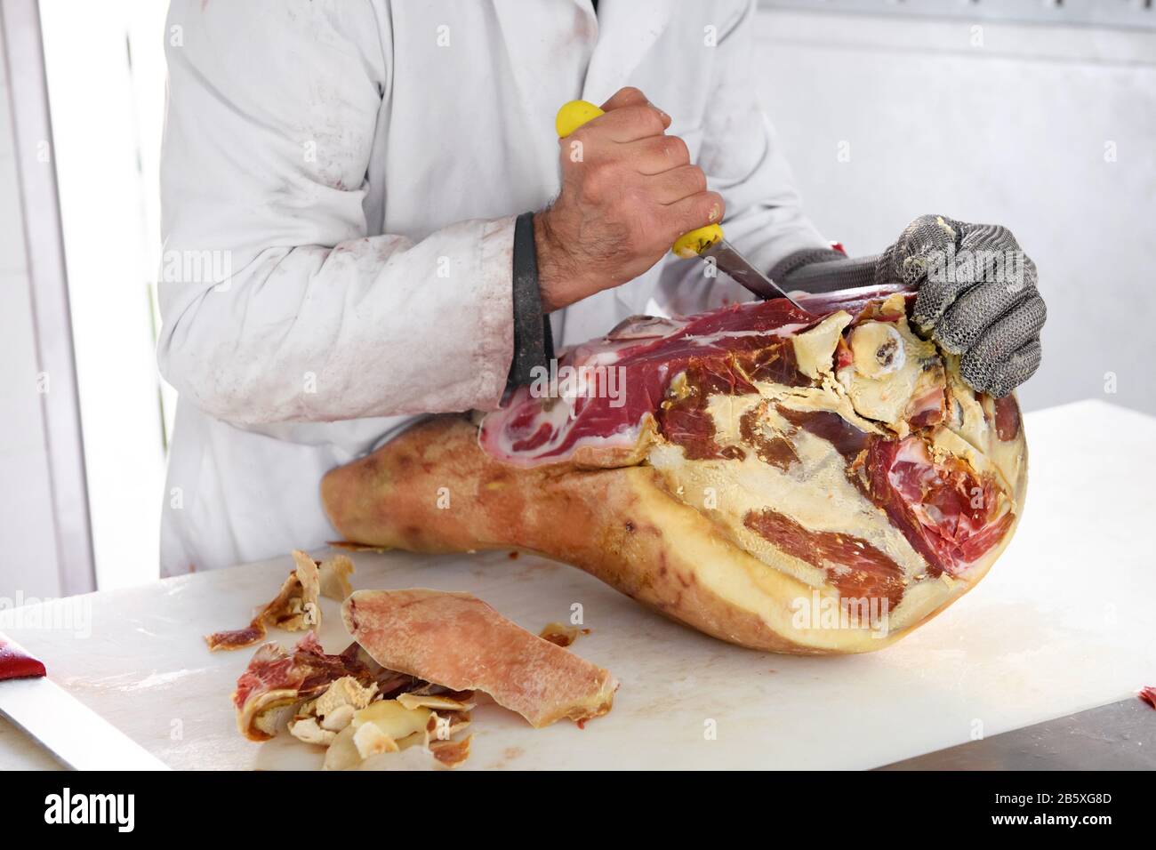 Boucherie désobéissant un jambon prosciutto italien avec un couteau tranchant dans une boucherie ou un magasin dans une vue rapprochée est mains, une dans un gant de fer de protection Banque D'Images