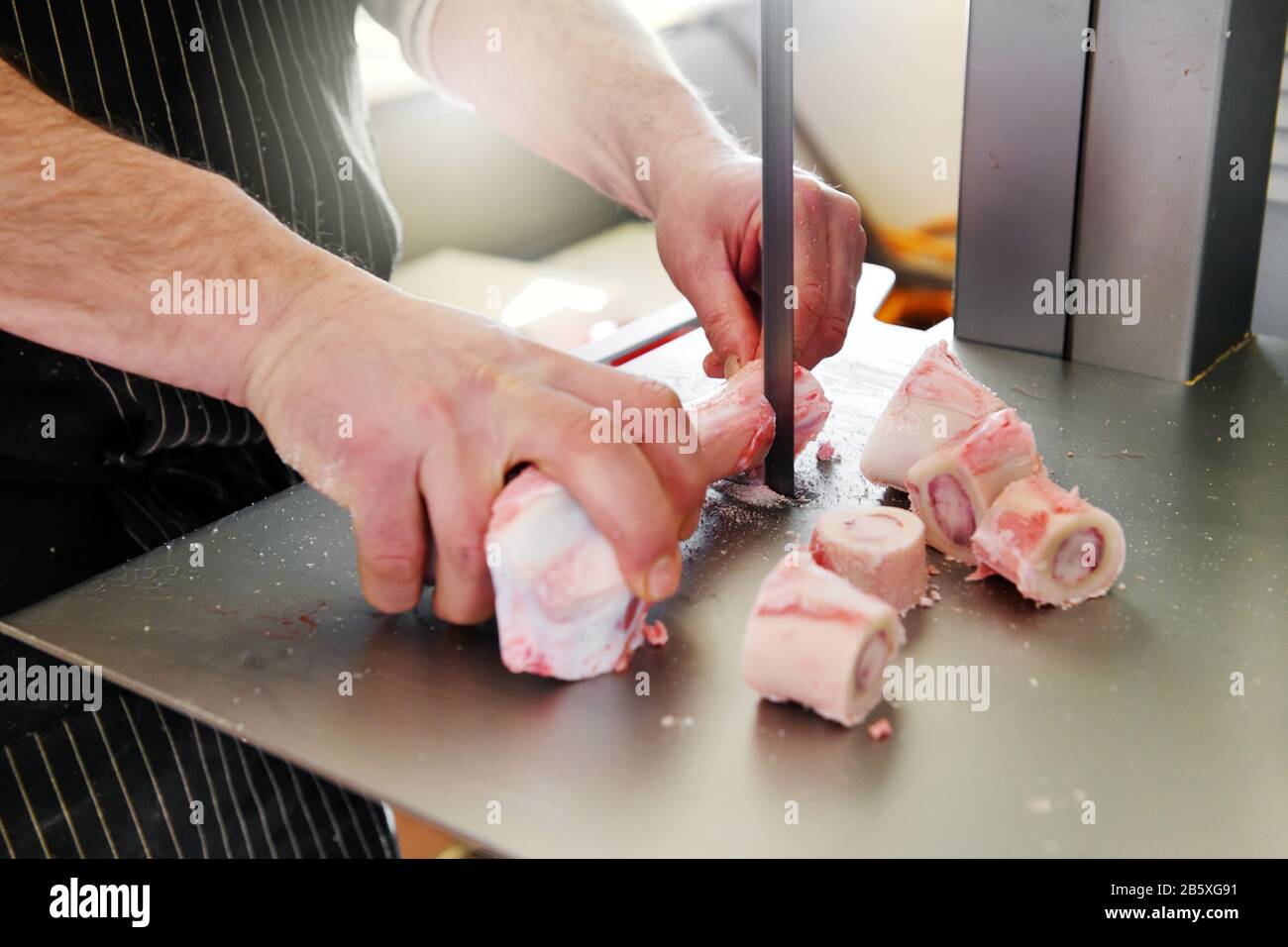 Boucherie sciant des os de moelle d'un fémur de veau à l'aide d'une scie à ruban dans la boucherie en gros plan sur ses mains Banque D'Images