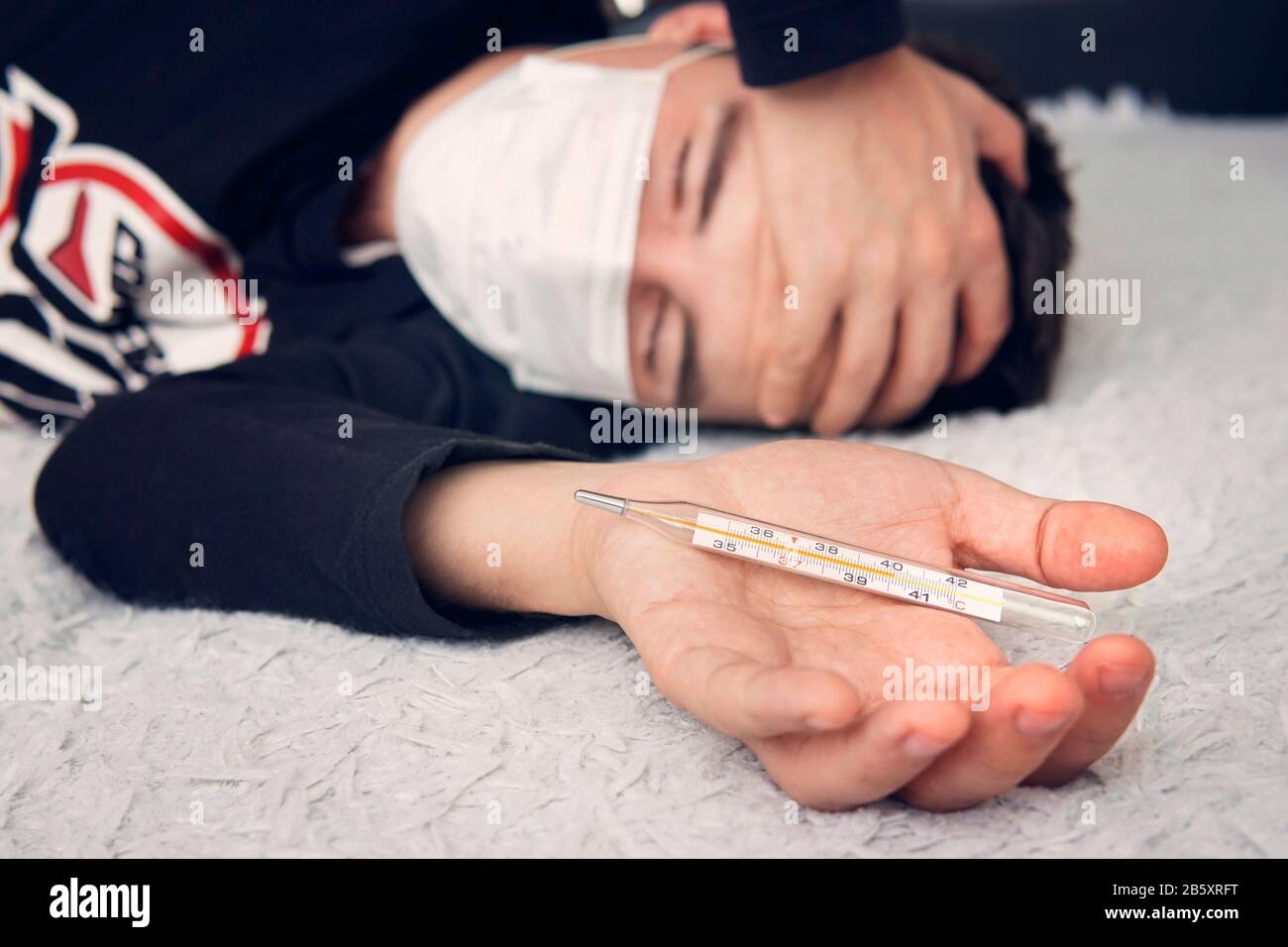 Homme malade avec une forte fièvre et un thermomètre. Le gars est allongé sur le lit tenant une tête douloureuse, un thermomètre dans sa main . Banque D'Images