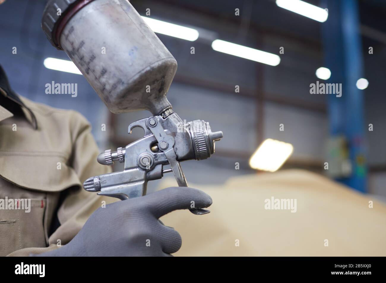 Gros plan horizontal de la main de l'homme non reconnaissable dans le gant tenant pistolet vaporisateur avec peinture, espace de copie Banque D'Images