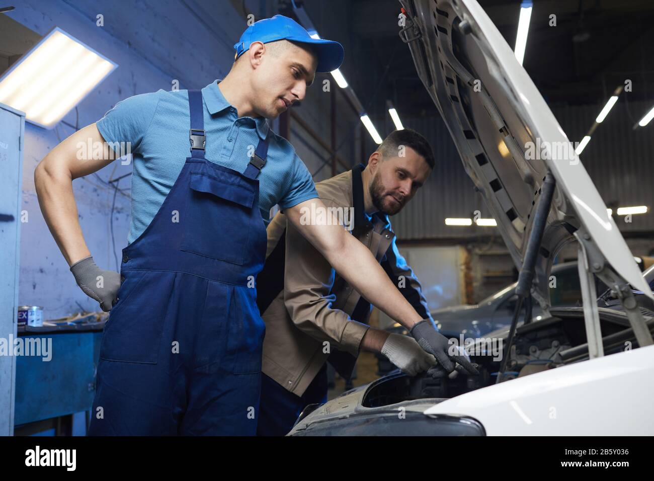 Prise de vue horizontale moyenne à faible angle de deux mécaniciens d'automobile professionnels portant un contrôle uniforme de la santé du véhicule ensemble, espace de copie Banque D'Images